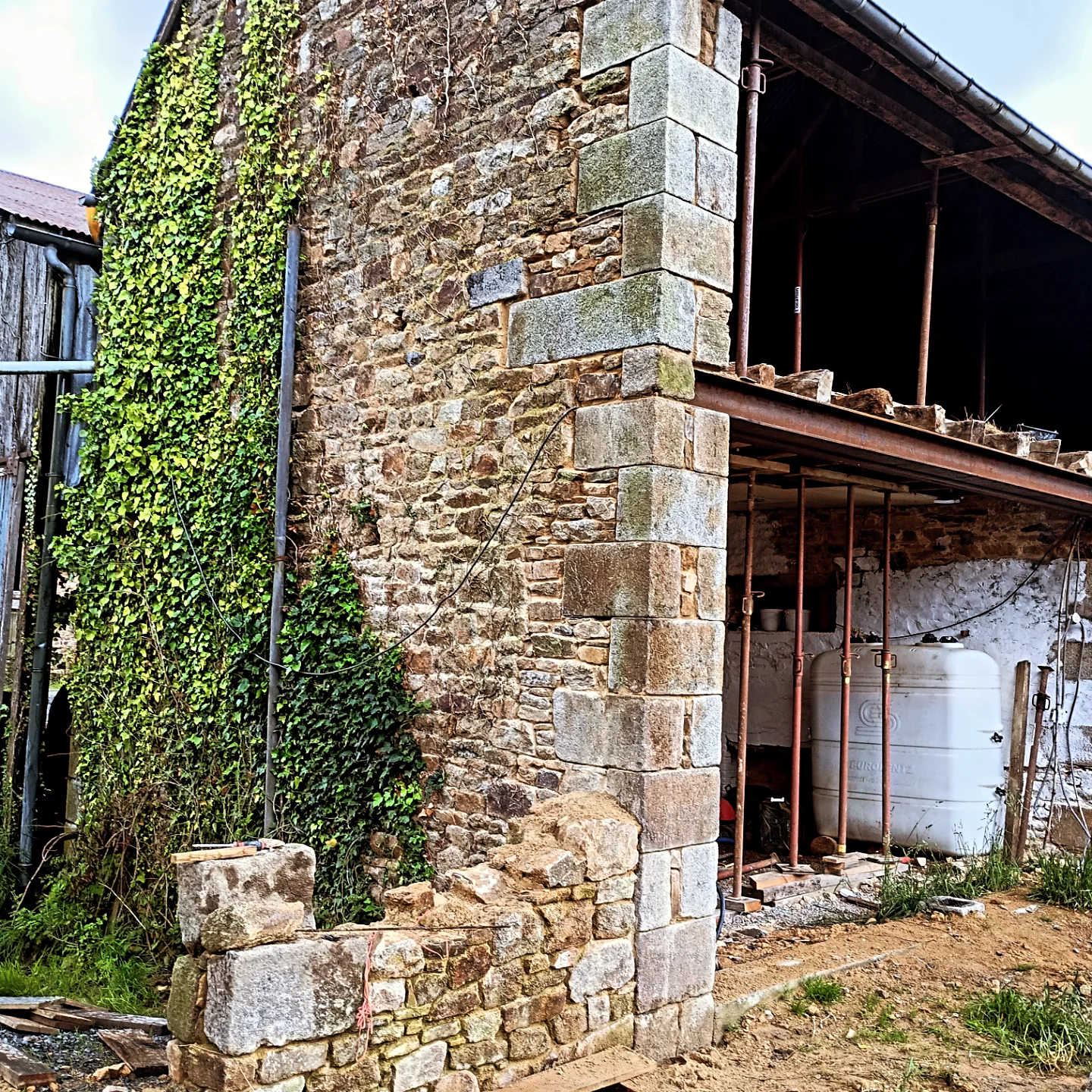 Mur en pierre ancien restauré avec chaînage d'angle en granit